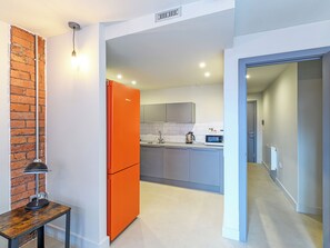 Una cocina moderna con armarios grises, un refrigerador rojo y una pequeña mesa con una lámpara.
