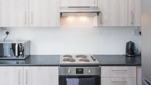 A kitchen with light wood cabinets, a built-in microwave, a stove, and a kettle. - Newport House Crindau Road Upper (Newport)