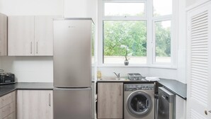 A compact kitchen with a stainless steel refrigerator, a washing machine, and a toaster. - Newport House Crindau Road Upper (Newport)