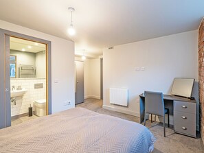 A bedroom with a bed, a desk, a chair, a radiator, and a bathroom visible through an open door. - Apartment 16-UK42640 (Preston)