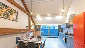 Una cocina moderna con un refrigerador rojo brillante, vigas de madera y un comedor con mesa dispuesta para cuatro.
