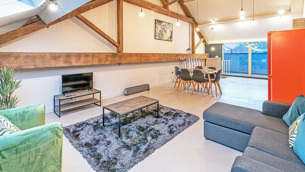Un loft amplio con techos altos, vigas de madera a la vista, un comedor con mesa y sillas, un televisor y un sofá.