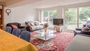 Een ruime woonkamer met een groot raam, een flatscreen televisie en een gezellige zithoek met een salontafel.