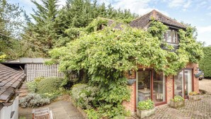 Een huis met een bakstenen gevel, een overdekte veranda en een tuin met diverse planten en een bankje.