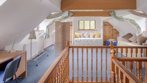 Een gezellige slaapkamer onder de dakpannen met een houten bureau, een bed met veel kussens en een raam dat voor natuurlijk licht zorgt.