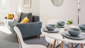 Ett modernt vardagsrum med en grå soffa, ett vitt matbord med grå skålar och tallrikar samt en liten krukväxt.