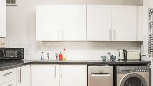Ett kompakt kök med vita skåp, en mikrovågsugn, en diskmaskin och en tvättmaskin.