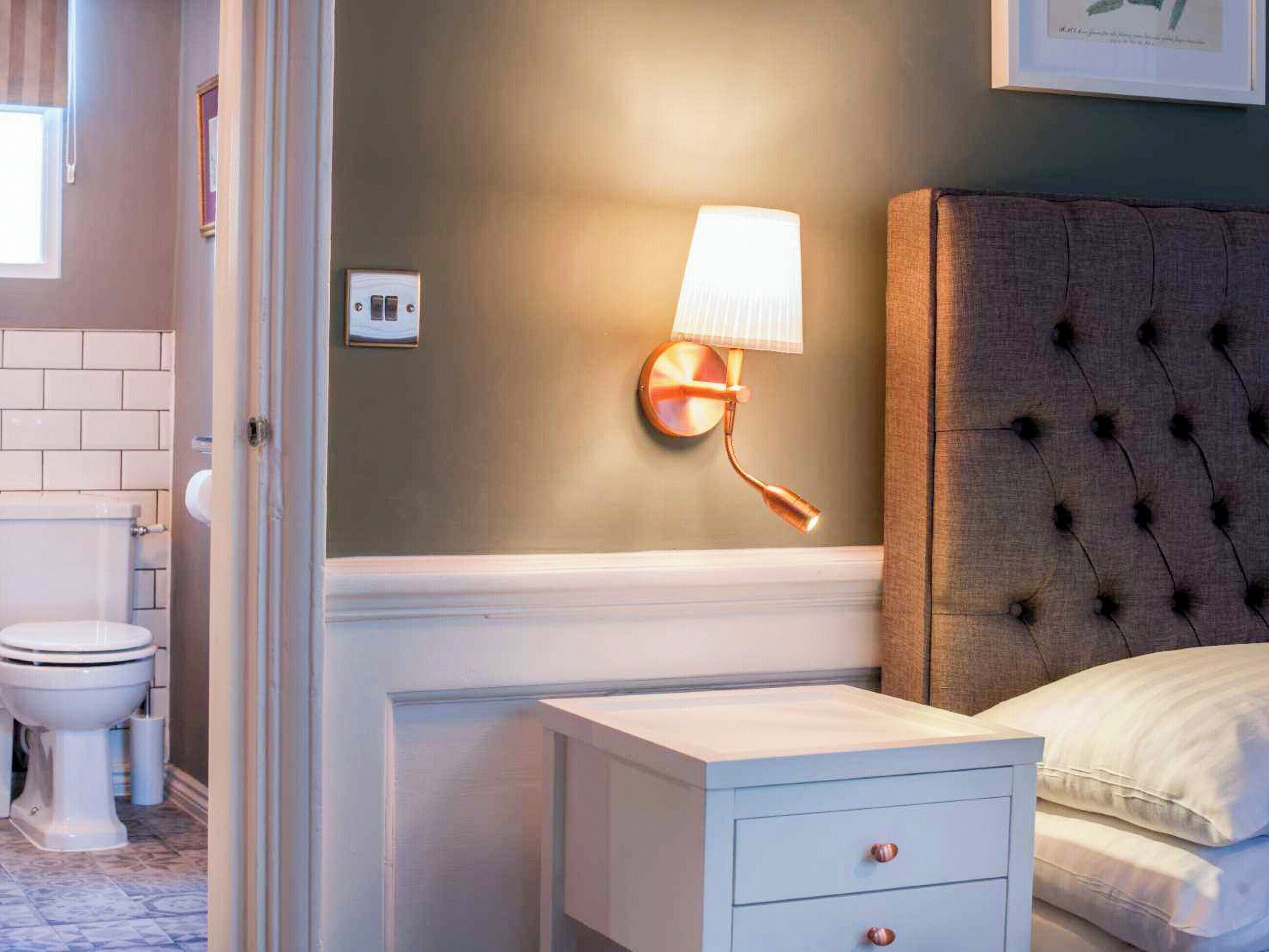 A bathroom with a toilet, a white sink, a mirror, and a wall-mounted light fixture.