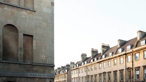 En byggnad med en skylt som visar texten ”BROAD-STREET” och en rad traditionella byggnader med många fönster och skorstenar.