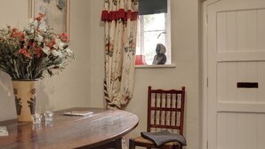 A dining area with a wooden table, a vase of flowers, a chair, and a window with a view of a statue. - 2 bedroom accommodation in Near Cheltenham (Near Cheltenham)