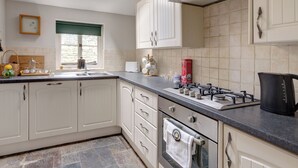 A modern kitchen with white cabinets, a gas stove, a built-in oven, and a window with a view. - 2 bedroom accommodation in Near Cheltenham (Near Cheltenham)