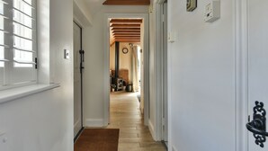 Ein Flur mit Holzbalken an der Decke, einer weißen Tür links und einer braunen Fußmatte am Eingang.