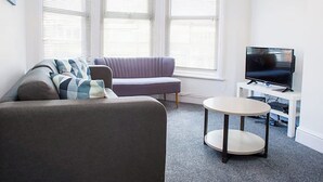 A modern living room with a grey sofa, a round coffee table, and a flat-screen TV. - Shirehampton Apartment (Shirehampton)