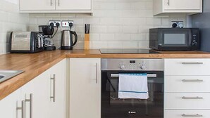 A kitchen with white cabinets, a wooden countertop, a coffee maker, a kettle, a microwave, and a Bosch oven. - Shirehampton Apartment (Shirehampton)