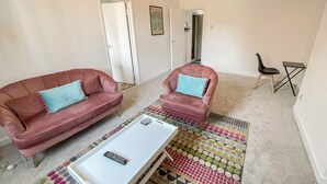 A living room with a red sofa, a matching armchair, a coffee table, and a colorful rug. - 2 bedroom accommodation in Bristol (Bristol)