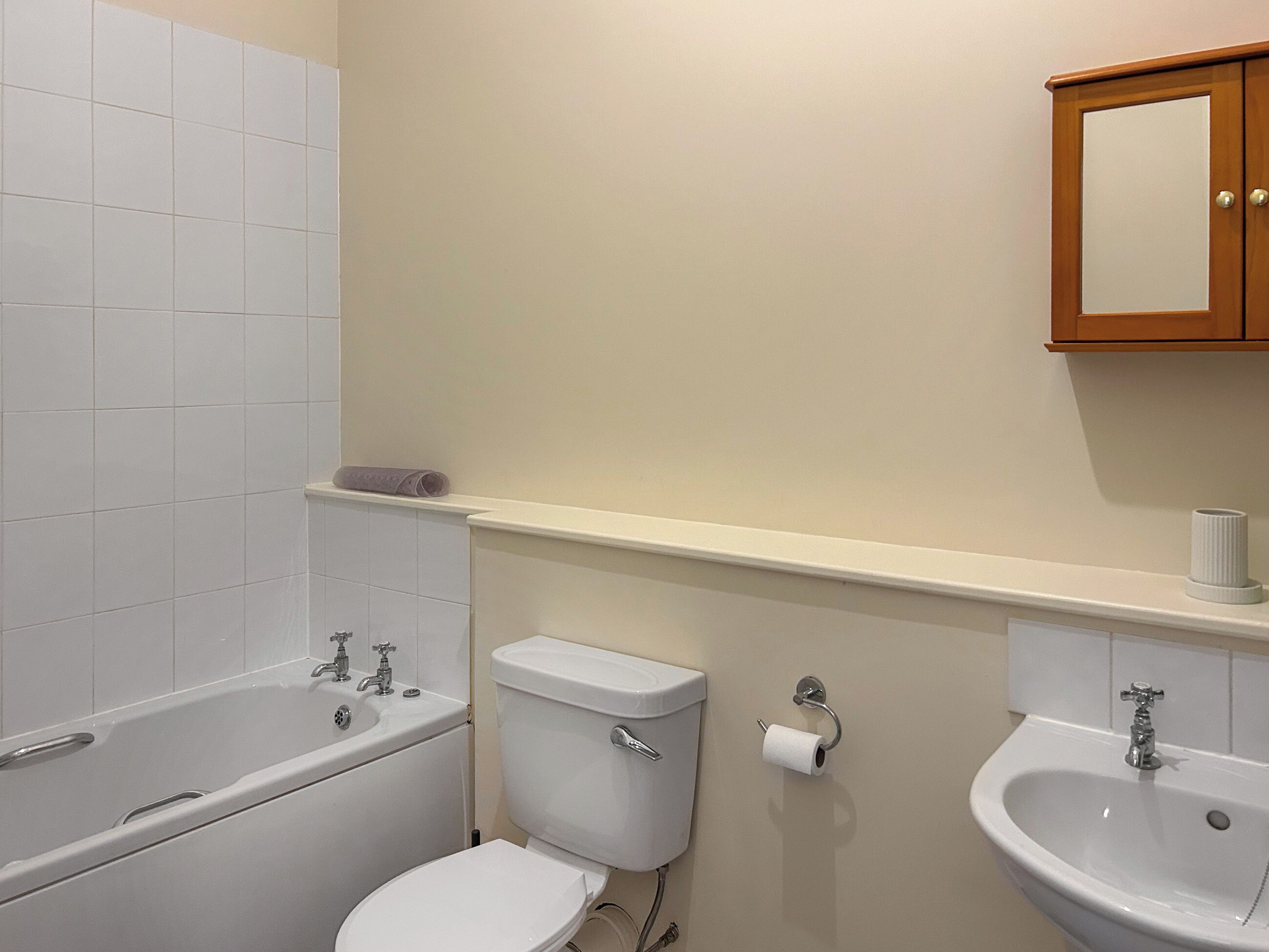 A bathroom with a bathtub, toilet, sink, and a mirror above the sink.