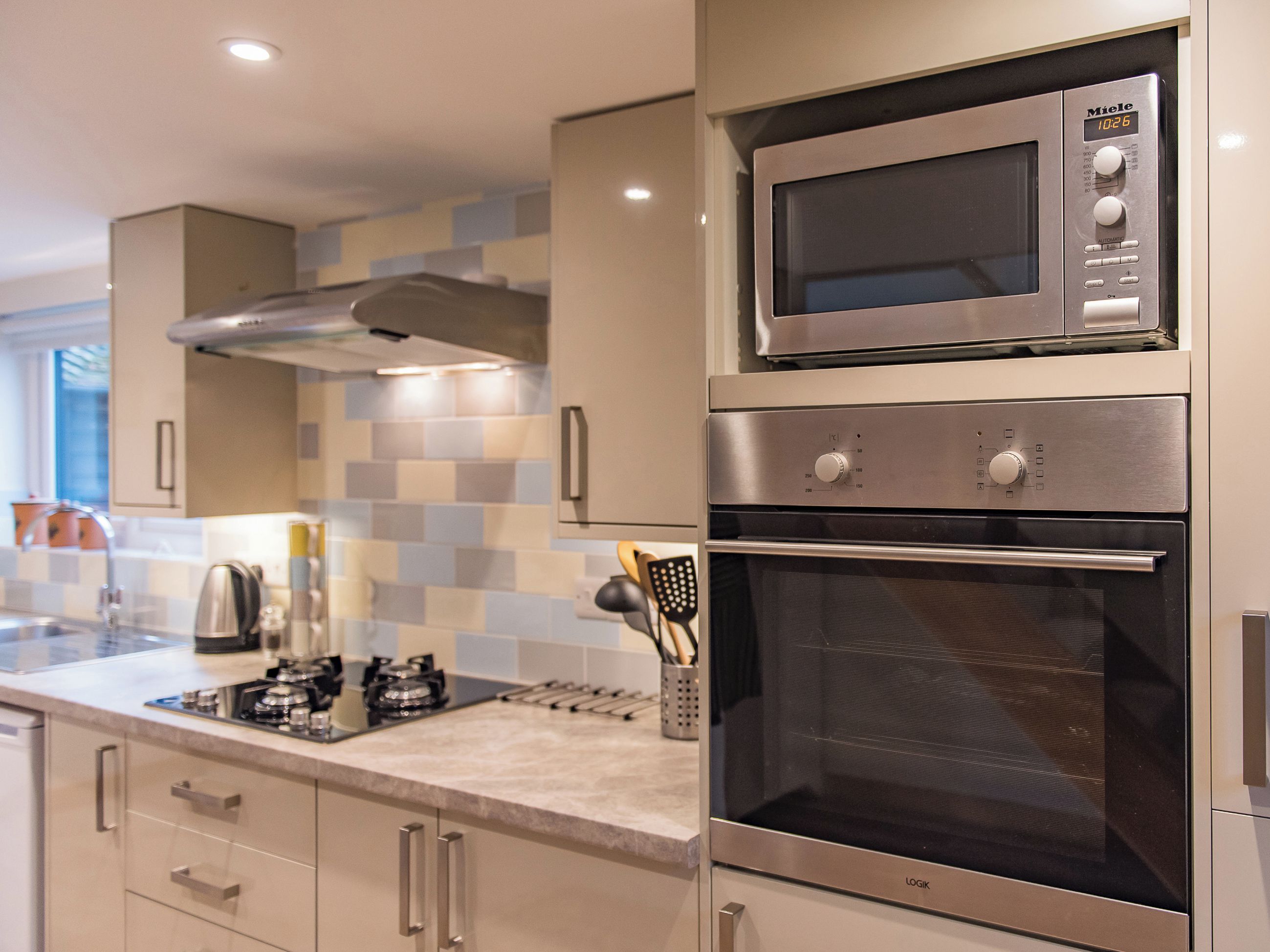 Uma cozinha moderna com eletrodomésticos de aço inoxidável, incluindo micro-ondas e forno, e painel de azulejos na parede.