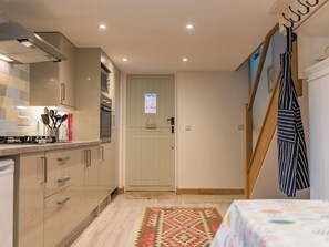 A compact kitchen with modern appliances, a wooden door with a 'Please remove your shoes' sign, and a striped towel hanging on the wall. - 1 bedroom accommodation in Biddenden, near Ashford (Biddenden, near Ashford)