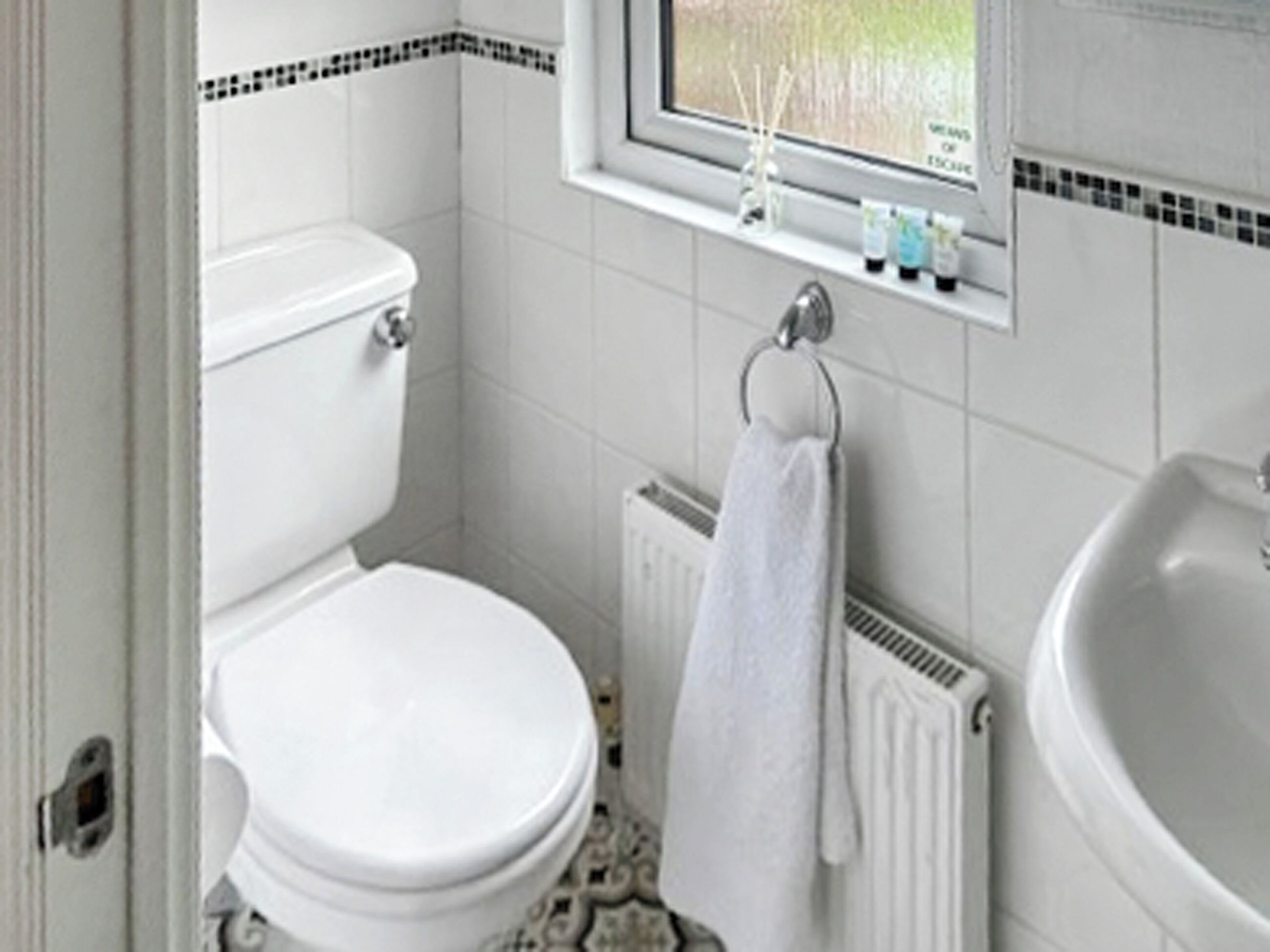 A small bathroom with a toilet, a radiator, a sink, and a window with a view of greenery.