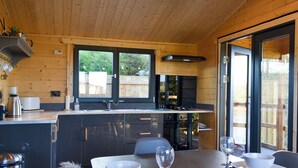 Una cocina moderna con paredes de madera, un ventanal grande y una zona de comedor con una mesa dispuesta para dos.