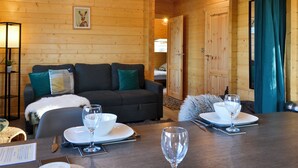 Interior acogedor de una cabaña de madera con sofá, mesa de comedor preparada para dos personas y un cuadro en la pared.