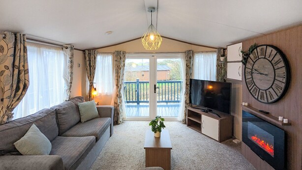 A living room with a sofa, TV, fireplace, and a balcony with a view. - Riverside Retreat - UK51191 (Morpeth)