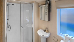 A bathroom with a glass-enclosed shower, a pedestal sink, and a window with toilet paper. - Riverside Retreat - UK51191 (Morpeth)