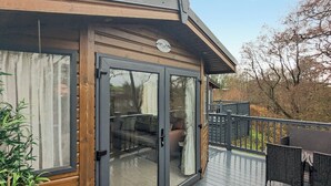 A wooden deck with a glass door leading to a covered outdoor seating area. - Riverside Retreat - UK51191 (Morpeth)