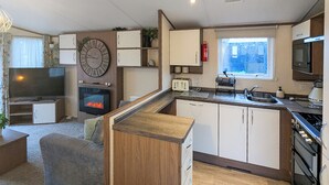 A compact living space with a kitchenette, a television, a fireplace, and a clock. - Riverside Retreat - UK51191 (Morpeth)