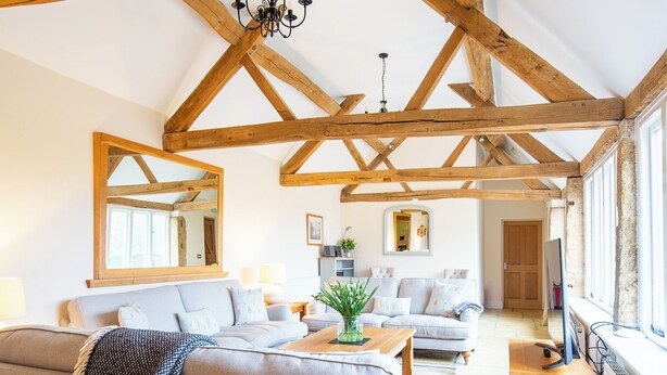 Ein geräumiges Wohnzimmer mit hohen Decken und freiliegenden Holzbalken, ausgestattet mit zwei Sofas, einem Couchtisch und einem Fernseher auf einem Holzboden.