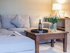 A living room with a grey sofa, a wooden coffee table with a wine bottle and glasses, a lamp, and a vase with flowers. - Great for families or friends looking looking for a spacious cottage. (Near Chipping Camden)
