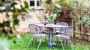 Un patio con pared de piedra, cerca de madera y una mesa con sillas.