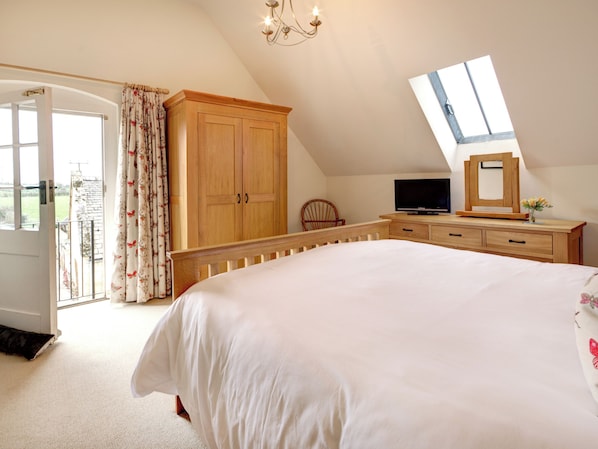 A bedroom with a large bed, wooden wardrobe, a television, and a skylight.