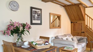 A cozy living room with a wooden table, a sofa, and a staircase. - 1 bedroom accommodation in Chipping Campden (Chipping Campden)