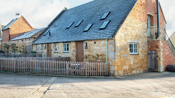 A stone building with a sloped roof, multiple windows, and a wooden fence in front. - 1 bedroom accommodation in Chipping Campden (Chipping Campden)
