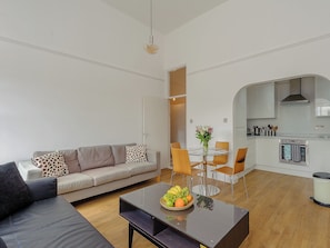 A modern living room with a sofa, a glass coffee table with fruit, and a dining area with chairs and a table.
