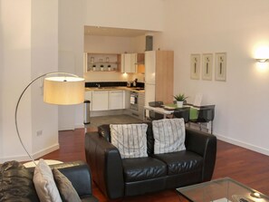 Ein Wohnzimmer mit einem schwarzen Ledersofa, einem Glastisch und einer Stehlampe.