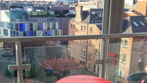Ein roter Tisch und Stühle auf einem Balkon mit Blick auf eine Stadtlandschaft.