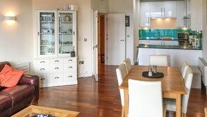 Ein Wohnzimmer mit braunem Ledersofa, einem Glastisch und einem Essbereich mit Holztisch und weißen Stühlen.