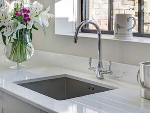 A kitchen with a white countertop, a stainless steel sink, and a vase with flowers. - The ultimate chic space for those seeking a stylish getaway. (Chipping Campden)