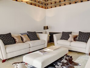 Ein Wohnzimmer mit zwei weißen Sofas, Kissen mit Muster, einem Couchtisch und einem Kuhfellteppich.