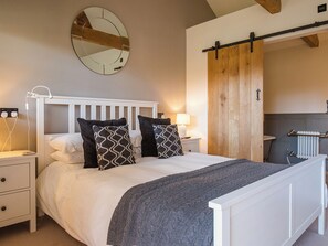 Ein Schlafzimmer mit einem weißen Bett, gestreiften Kissen, einem Nachttisch mit Lampe, einem Spiegel an der Wand und einer Holztür.