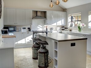 A modern kitchen with white cabinetry, a large island, and a gas stove. There are two vintage-style gas canisters on the floor. - The ultimate chic space for those seeking a stylish getaway. (Chipping Campden)