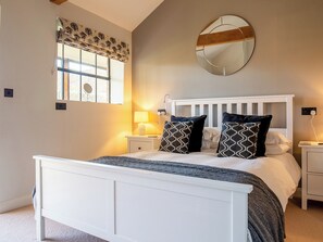 A bedroom with a white bed, patterned pillows, a bedside lamp, a round mirror, and a window with a tree-patterned valance. - The ultimate chic space for those seeking a stylish getaway. (Chipping Campden)
