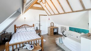 A bedroom with a sloped ceiling, a bed with a patterned bedspread, a wooden nightstand, a dresser, and a bathroom with a bathtub. - Sea Breeze - UK51253 (Kimmel Bay)