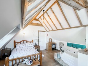 A bedroom with a sloped ceiling, a bed with a patterned bedspread, a wooden nightstand, a dresser, and a bathroom with a bathtub. - Sea Breeze - UK51253 (Kimmel Bay)