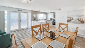 A dining area with a table set for six, wooden chairs, and a view of the kitchen in the background. - Sea Breeze - UK51253 (Kimmel Bay)