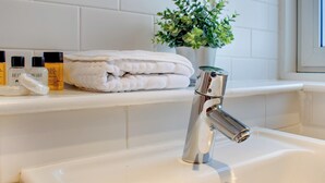 Une salle de bain avec un lavabo blanc, un robinet chromé moderne, des serviettes blanches soigneusement pliées et une petite plante en pot posée sur le comptoir.