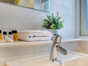 Un baño con un lavamanos blanco, un grifo cromado moderno, toallas blancas dobladas con pulcritud y una pequeña planta en maceta sobre el mostrador.