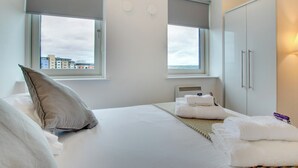Une chambre d’hôtel avec un lit, deux fenêtres équipées de stores, une armoire et une vue sur les bâtiments environnants.